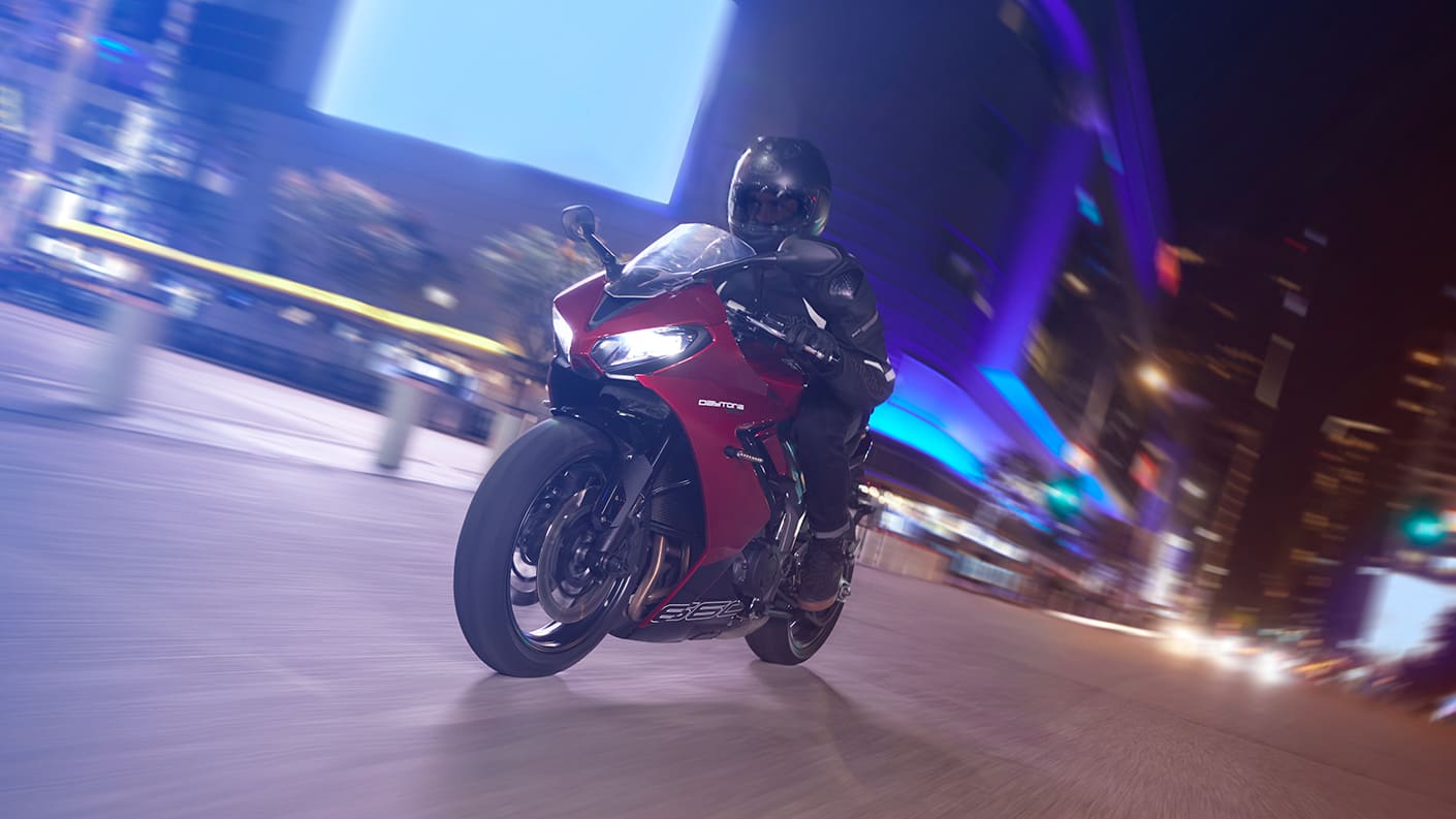 Triumph Daytona 660 in carnival red and sapphire black riding through city at night